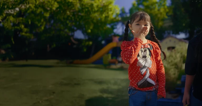 Niña tapandose la boca con la mano mientras juega en un patio verde