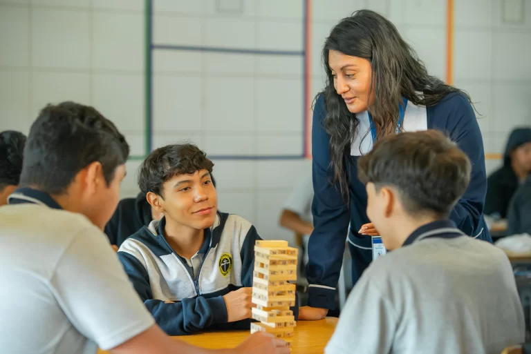 Profesora guiando a estudiantes mientras realizan actividad colaborativa en aula con juego educativo