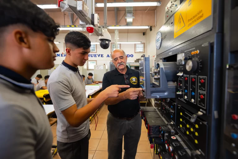 Profesor de formación técnica explicando el uso de maquinaria eléctrica a estudiantes en taller educativo